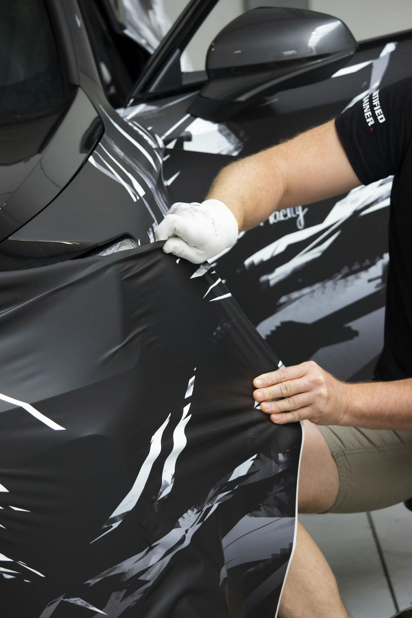 Man working in a garage, applying a vinyl wrap to a vehicle for customization.