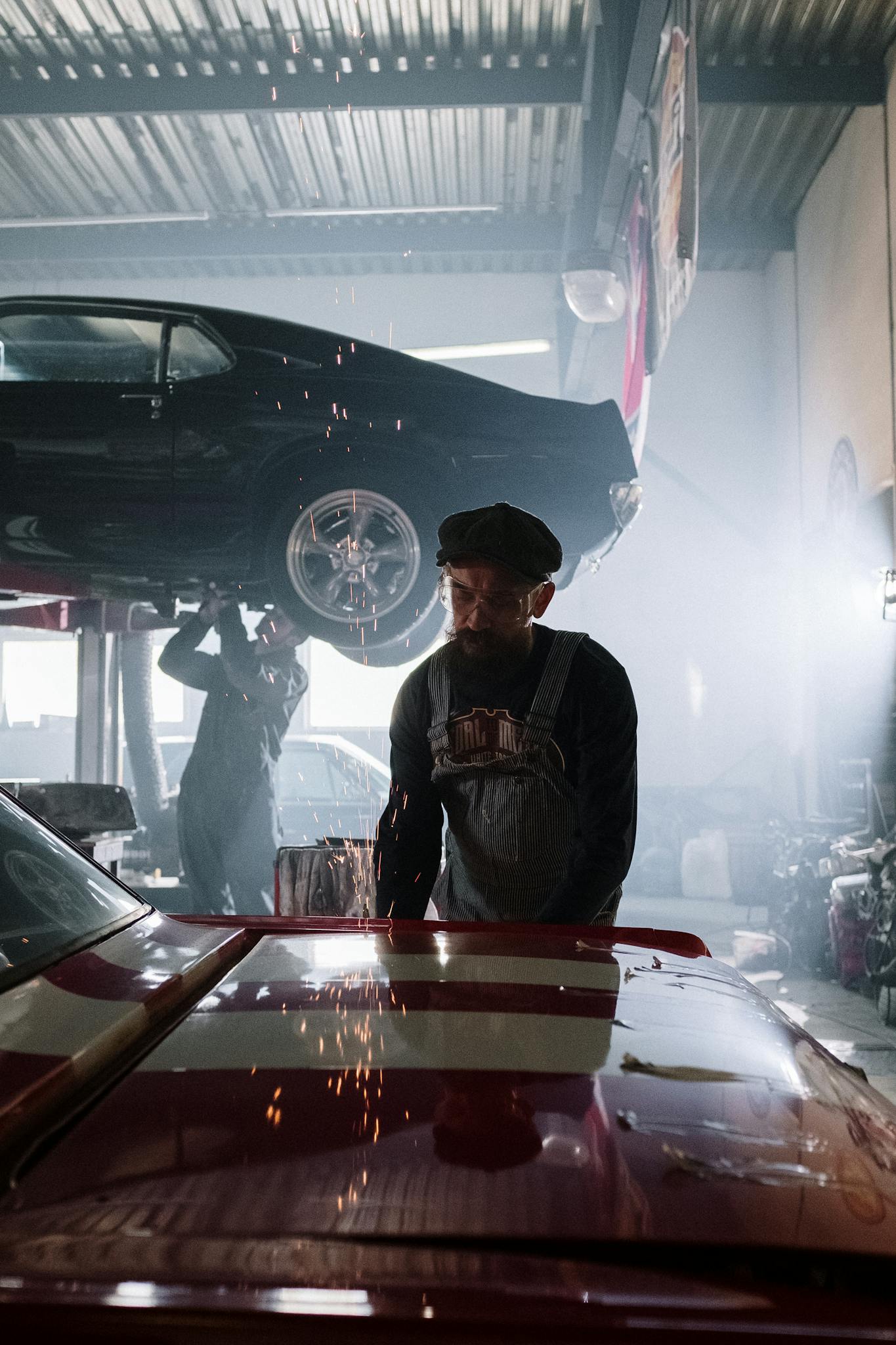 Mechanic working on vehicle with sparks flying in industrial auto repair shop.